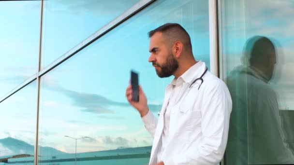 Młody Lekarz Rozmawiający Przez Telefon Przed Szpitalem — Wideo stockowe
