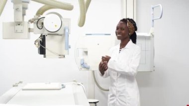 Bir röntgen odasında genç bir bayan doktor kameraya bakıp kollarını kavuşturuyor.
