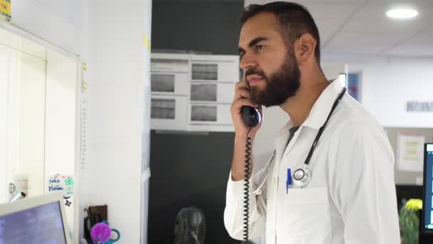 Νεαρός Άνδρας Γιατρός Μιλάει Τηλεφωνικά Στο Γραφείο Του — Αρχείο Βίντεο