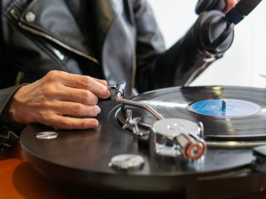 Kulaklığını takmak için deri ceket giyen bir kadın turntable 'ı plak çalarken...