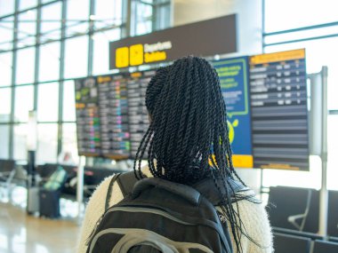 A young woman traveling alone checking the information on the airport screens.