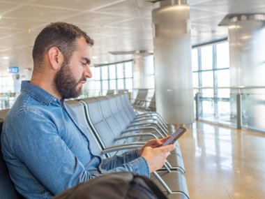 Bearded man using his smarphone while waiting in the airport terminal