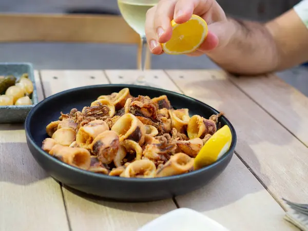 stock image A hand squeezing a lemon over a plate of fried squids