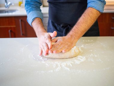 young man using his hands to knead a wheat flour dough clipart