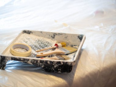 Boya fırçaları ve boya tepsisinde bir rulo maske bandı.