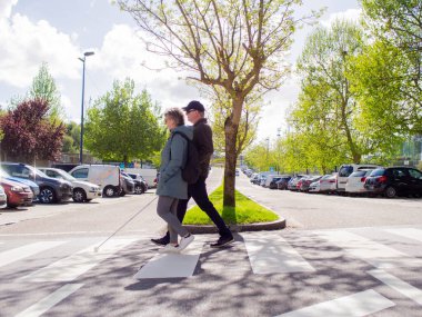Zebra geçidinde bastonuyla yürüyen kör bir adam ve yol gösteren bir kadının yan görüntüsü..