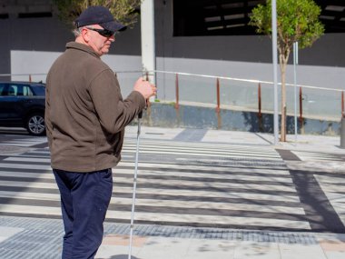 Kör bir adam sabırla yaya geçidinde karşıdan karşıya geçmek için bekliyor.