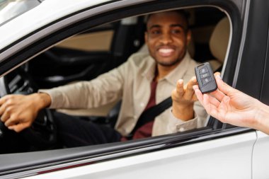 Yeni bir arabanın test sürüşü. Genç siyah adam sürücü koltuğunda otururken arabanın anahtarlarını alır. Yüksek kalite fotoğraf