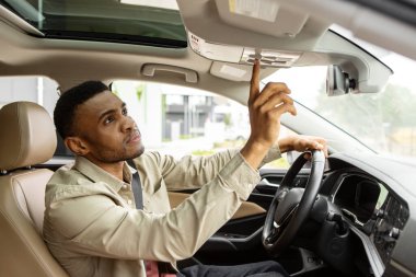African American man sitting in car pushing buttons, opening car sunroof or inspecting car, testing car in auto showroom. High quality photo clipart