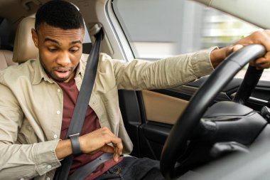 Afrika kökenli Amerikalı bir adam arabada sinirli bir ifadeyle kol saatine bakıyor. Yüksek kalite fotoğraf