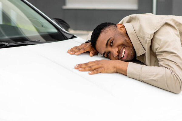 Новый владелец машины. Счастливый афроамериканец обнимает свой новенький автомобиль и покупает автомобиль в автосалоне. Селективный фокус. Высокое качество фото