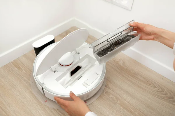 stock image The woman takes out the container and filter of the automatic robot vacuum cleaner to clean it of dirt and debris. High quality photo