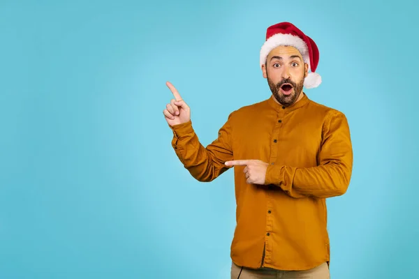 크리스마스 모자를 잘생긴 남자가 충격을 카메라를 손가락을 옆으로 향하고 고품질 — 스톡 사진