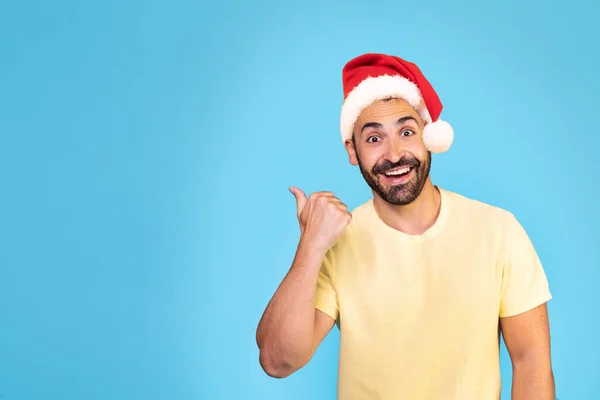 年轻的高加索人头戴圣诞帽 站在孤立的蓝色背景上 用拇指在复制空间中 高质量的照片 — 图库照片