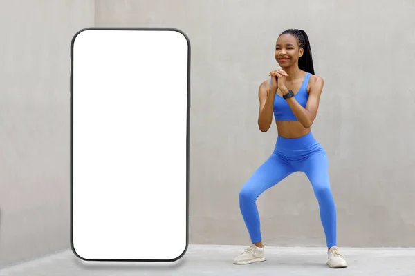 女运动员做蹲大旁边的巨型智能手机与灰色背景的空白白屏 介绍新的酷应用程序 免费复制空间模拟 网站设计横幅 高质量的照片 — 图库照片