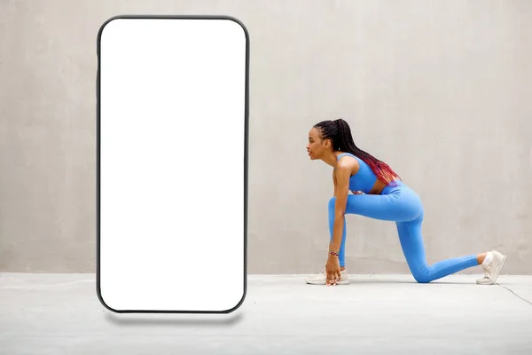 年轻女人在做伸展运动 健身模特早上在室外锻炼 旁边是一个巨大的智能手机 灰色背景上有一个空白的白色屏幕 没有复制空间 高质量的照片 — 图库照片