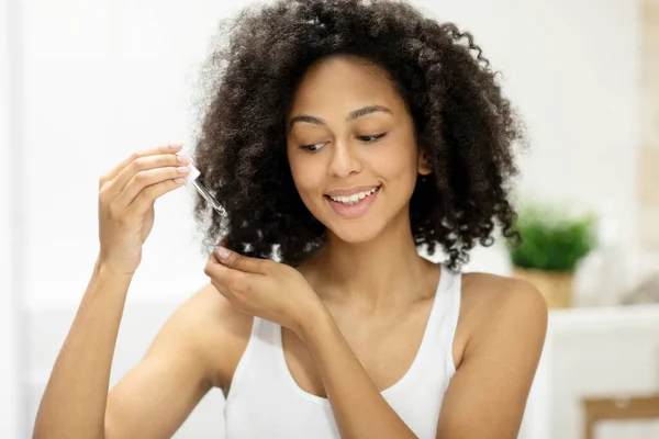 Split Ends Treatment. African American Woman Applying Serum On Damaged Dry Hair In Modern Bathroom At Home. Cosmetics For Hair Repair, Haircare And Beauty Care Routine Concept. High quality photo