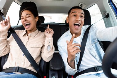 Neşeli siyahi kadın ve erkek şarkı söylüyor, dans ediyor ve arabada seyahat etmekten keyif alıyor, keyifli olmak, yeni bir araba almak, hafta sonu gezisi ve yolculukta yol almak