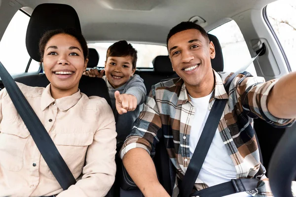 Excited multiracial family driving auto, boy pointing finger showing destination of road trip, traveling on vacation by car and enjoying ride