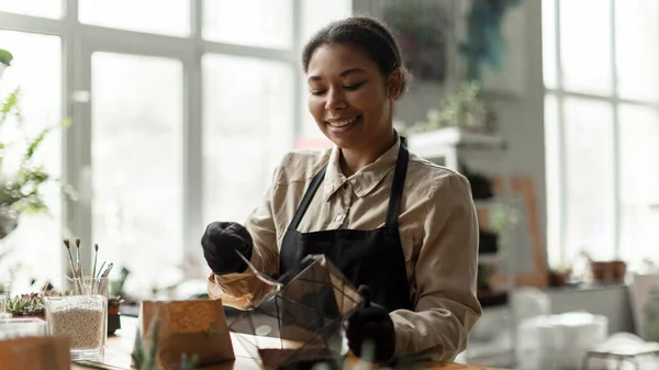 stock image DIY florarium concept. Skilled florist woman pouring soil in glass geometric shape vase, creating botany art composition with mini plants, working at her own greenhouse