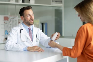 Doktor, klinikten sonra kadın hastaya reçete yazıyor. Erkek terapist, genç kadına vitamin veriyor.