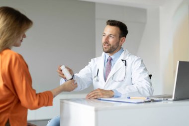 Doktor, klinikten sonra kadın hastaya reçete yazıyor. Erkek terapist, genç kadına vitamin veriyor.