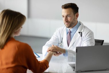 Stresli genç bayan hastayı rahatlatan düşünceli erkek doktor zor tanı konusunda kötü haber alıyor, klinikte oturuyor.