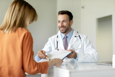 Danışman hasta. Tedavi öneren neşeli erkek doktor klinikteki sağlık kontrolü sırasında kadın hastaya terapi detaylarını açıklıyor.