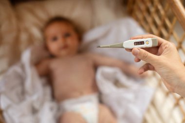 Anne termometreyi bebeğin arka planında 39.9 derecelik bir işaretle tutuyor. Çocuk hastalıkları, yüksek vücut sıcaklığı.