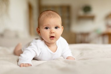 Çocuk bakımı konsepti. Evdeki çarşafların üzerine uzanmış şirin bebek portresi yatak odasında emekleyen bebek, bedava fotokopi alanı.