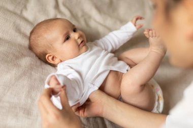 Anne uyandıktan sonra küçük bebeğini giydirip giydiriyor. Vücut giysisini giydiriyor. Çocuk evde, gözünün önünde yatıyor. Anne ve çocuk kavramı