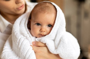 Anne, havluya sarılıp kameraya bakarak banyo yaptıktan sonra bebeğine sarılıyor. Çocuk bakımı rutini. Anne ve bebek