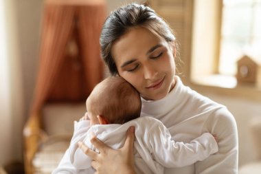 Anne ve bebek arasında bir bağ. Anne küçük çocuğuna sarılıyor, evdeki rahat yatak odasında bebekle bağ kuruyor. Annelik ve ebeveynlik konsepti