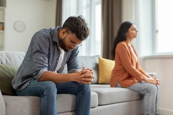 Unhappy indian man and woman sitting on sofa, husband and wife feeling down after quarrel, spouses thinking about divorce, need for family therapy