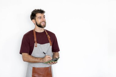 Önlük takan mutlu barista adam, not defterine sipariş menüsü yazıyor beyaz arka planda boş alana bakıyor.