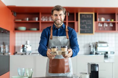 Kahve fincanı kutusu tutan neşeli Avrupalı bir adamın portresi ve sipariş verme, kameraya bakıp gülümseme, kafede dikilme.