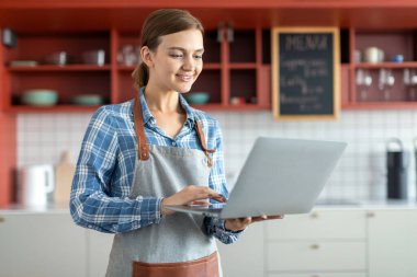 Kafe sahibi, gülümseyen beyaz kadın baristanın portresi. Kapalı mekanlarda dizüstü bilgisayarda çalışıyor. Bilgisayarda siparişleri işliyor.