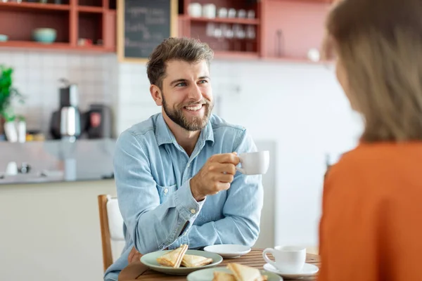 Happy young european couple talking over a cup of coffee at cafe, man and woman sitting at coffee shop having a conversation while having coffee