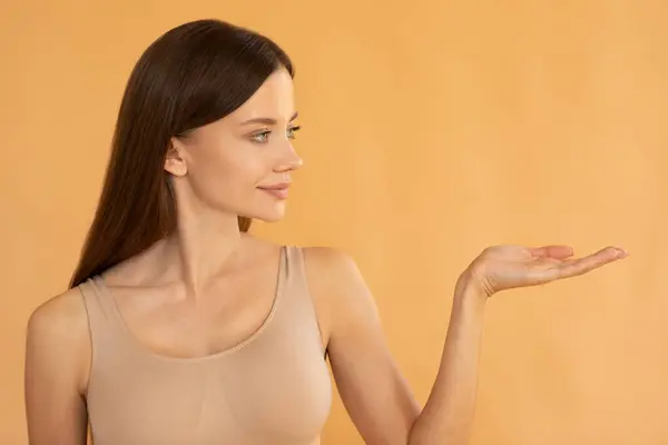 Beauty ad. Young lady holding something on empty palm, demonstrating copy space for advertisement and design on peach background
