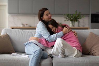 Sevgi dolu anne genç kızı kucaklıyor, anne üzgün genç kıza anlayış gösteriyor ve destek oluyor, evde kanepede birlikte oturuyor.