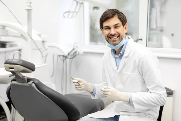 Cheerful male dental doctor holding dental equipment for work and smiling at camera in dentistry clinic. Concept of stomatology, dentistry and orthodontics