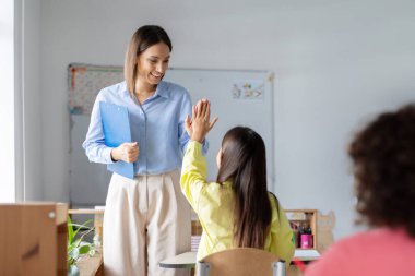 Masada oturan öğrenciye gülümseyen beyaz kadın öğretmen beşlik çakıyor. Eğitim, çocukluk, öğretim, öğrenme ve okul kavramı