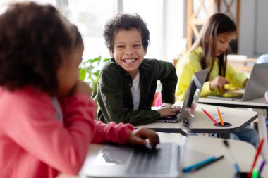 Öğrenci sınıfta dizüstü bilgisayar kullanıyor, aktif olarak arkadaşlarıyla tartışıyor ve işbirliği yapıyor, interaktif öğrenme çağdaş yaklaşımını vurguluyor