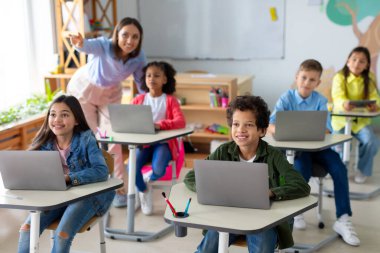 Dizüstü bilgisayar kullanan okul çocukları, bilgisayar bilimleri dersinde sınav sırasında tahtaya işaret eden kadın öğretmenler. Modern eğitim