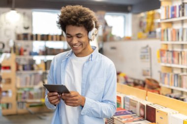 Siyahi öğrenci kütüphanede çalışıyor, kulaklık takıyor, tablet kullanıyor, modern öğrenim ve konsantrasyon sahneleri yaratıyor.