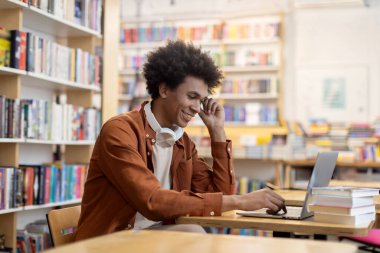 Kütüphanede dizüstü bilgisayar kullanan Afrikalı Amerikalı öğrenci, çevrimiçi ya da test için hazırlanıyor, odaklanmış ve teknoloji odaklı akademik çabaları tasvir eden sahne