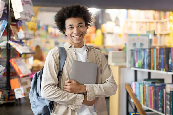 Exuding success, black student with backpack beams while holding copybooks in the library, symbolizing achievement, determination, and joy of educational triumph