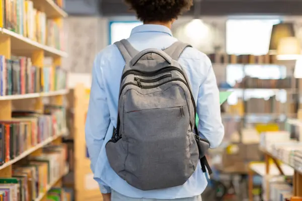 Back view of male student wearing backpack, standing in library, showcasing moment of reflection and preparation for an immersive study session