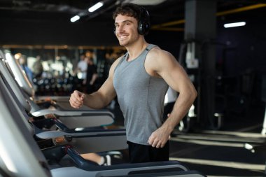 Koşu antrenmanı. Spor salonunda koşu bandında koşan kablosuz kulaklıklı mutlu adam spor giyim sektöründe motive olmuş adam spor salonunda vakit geçiriyor.