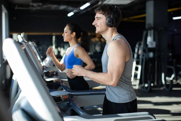 Strong man and fit woman running on treadmills or running machine in modern fitness gym, couple focusing on running, enjoying workout